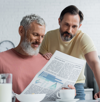 Same sex couple looking over the newspaper together at the kitchen table.